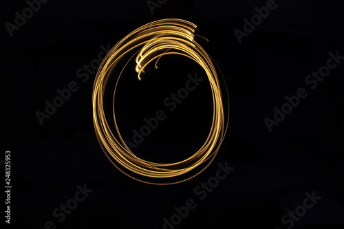 Long exposure, light painting photography.  Letter o in a vibrant neon metallic yellow gold colour against a black background.  Alphabet series. photo
