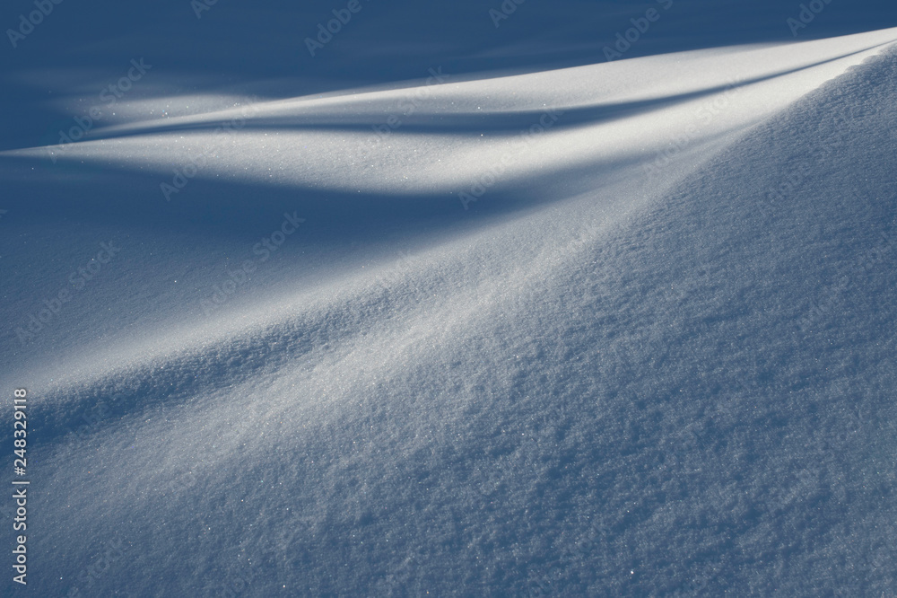 A texture of a small, snow covered hill in a cold environment with a contrast of light and shadow.