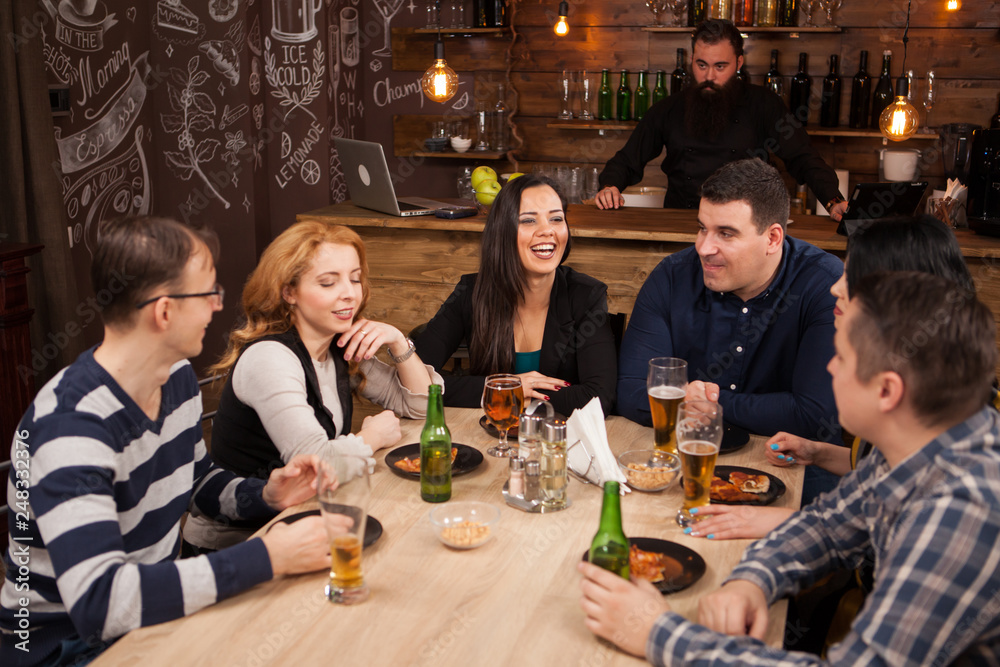 Group of young friends sitting around table in bar togethe