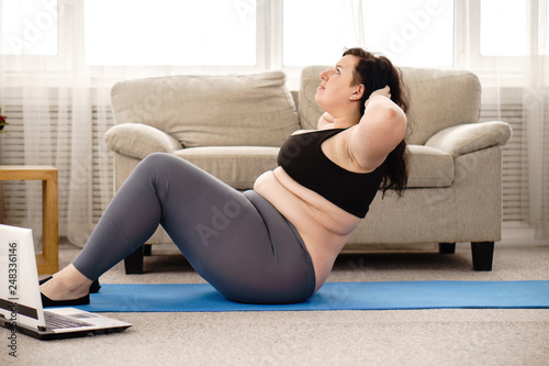 fitness, sport, weight loss, exercising, home workout, training, lifestyle. young plus size woman doing sit-ups on mat at home