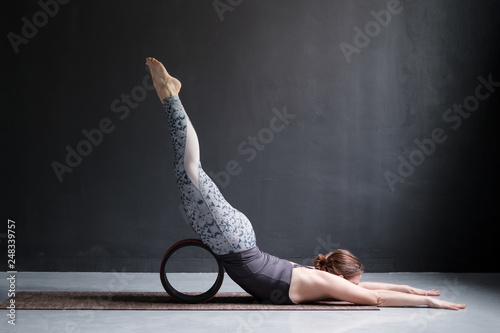 Woman practicing yoga doing Shalabhasana using wheel, Locust pose in full length photo