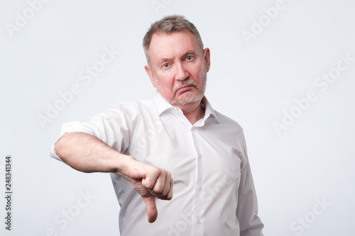 Senior man in white shirt giving thumb down