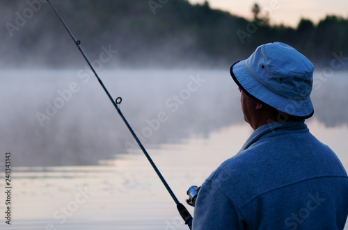 Caucasian fisherman, 50's, at the lake with fog, early morning just before sunrise. © Studio Specialty