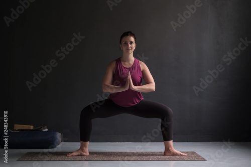 Beautiful young yoga model working out indoor doing Goddess or Sumo Squat Pose