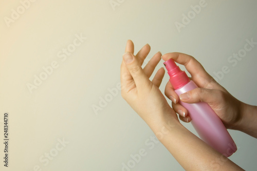 Female hand holdinc cosmetical pink bottle spray, isolated. Sunscreen protection, skin care, beauty and cosmetology. Copy space.