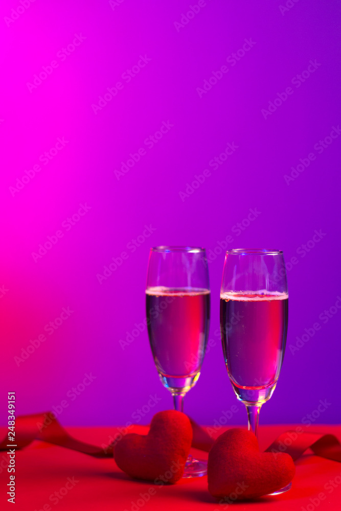 Champagne in glasses of two in romantic valentine concept with heart shaped fabric on red and purple background Champagne in glasses of two in romantic valentine concept with heart shaped fabric on red and purple background