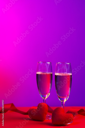 Champagne in glasses of two in romantic valentine concept with heart shaped fabric on red and purple background