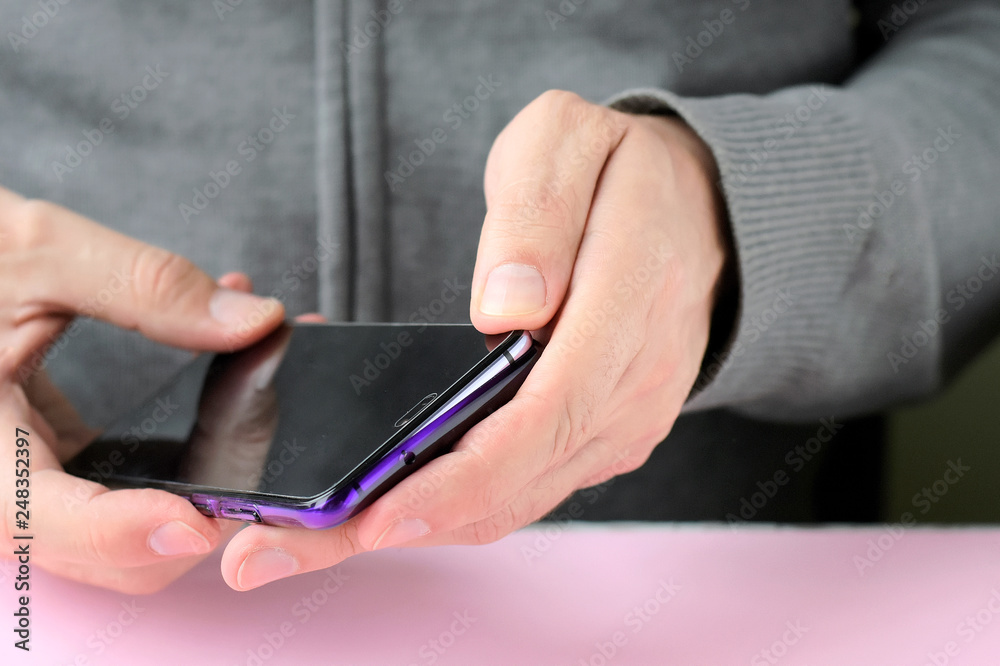 Male hands are holding a phone and putting on a shiny colorful cover. White man in a gray sweater put on a new violet case on smartphone with selective focus. Plastic case for digital gadget Male hands are holding a phone and putting on a shiny colorful cover. White man in a gray sweater put on a new violet case on smartphone with selective focus. Plastic case for digital gadget