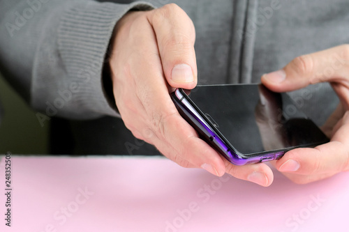 Male hands are holding a phone and putting on a shiny colorful cover. White man in a gray sweater put on a new violet case on smartphone with selective focus. Plastic case for digital gadget