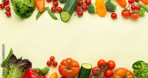 Raw vegetables background, tomatoes cucumbers lettuce pepper spring onion broccoli peas on light yellow table, top view, copy space, selective focus