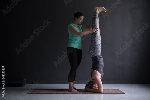 yoga instructor helping female student with headstand pose, salamba sirsasana