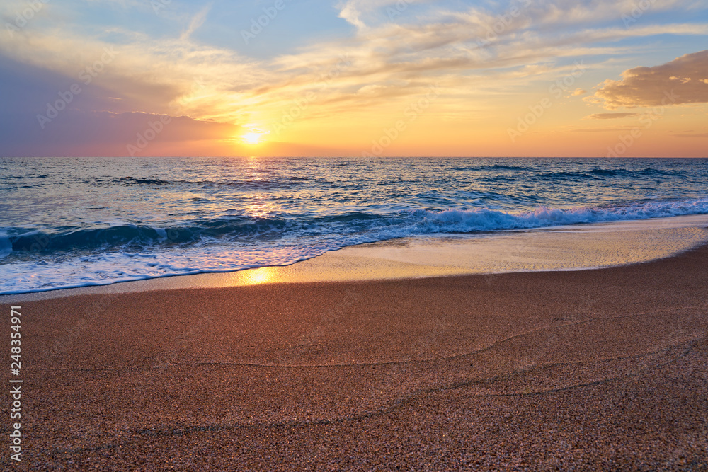 Colorful sunset at the tropical beach, sun behind clouds reflects on water and waves with foam hitting sand. Colorful sunset at the tropical beach, sun behind clouds reflects on water and waves with foam hitting sand.