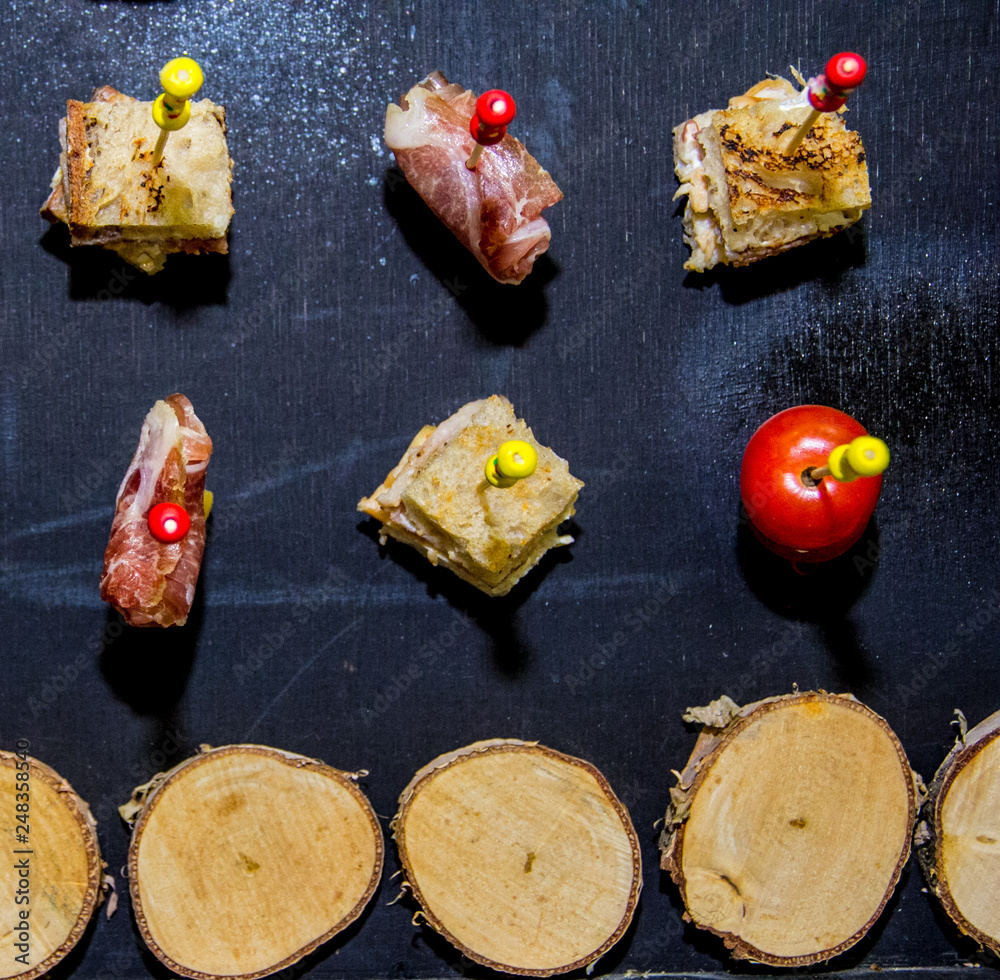 Plakat Skewers with food bread bacon and tomatoes on black background with wooden log cabins