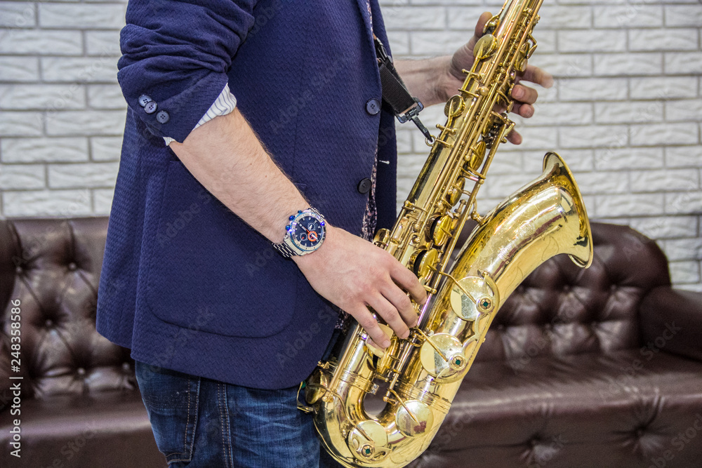 Fototapeta premium men's hands holding a saxophone against a white wall and a leather sofa