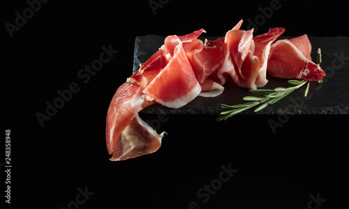 Prosciutto with rosemary on a black background.