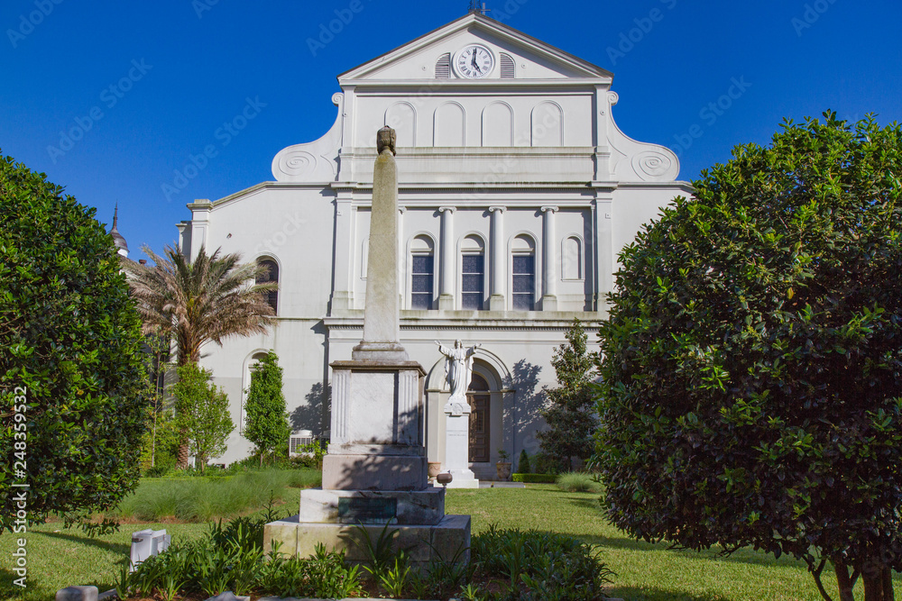 Rear view of St. Louis Cathedral, New Orleans, Louisiana, USA. Statue of Christ with open arms in garden behind church. Green grass and blue sky