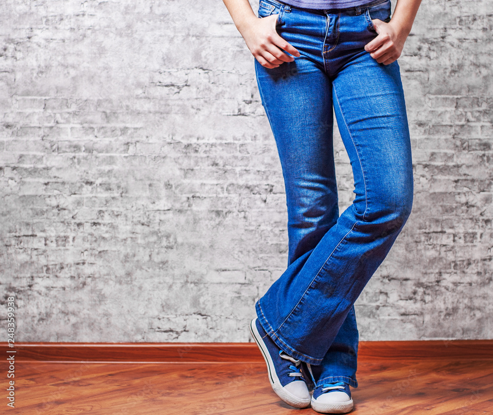 Woman fashion concept. Female legs in jeans and sneakers on gray wall background with copy space Woman fashion concept. Female legs in jeans and sneakers on gray wall background with copy space