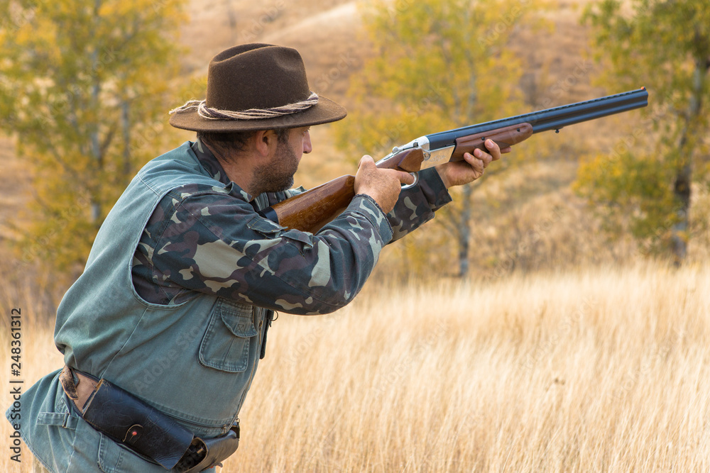 Fototapeta premium Hunter with a hat and a gun in search of prey in the steppe 
