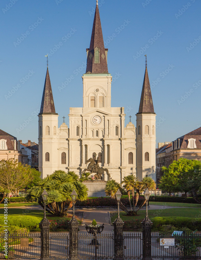 St. Louis Cathedral at sunrise with statue of Andrew Jackson in front and American flag on right side, in the French Quarter of New Orleans, Louisiana, USA. Clear blue sky, no people, horizontal. 