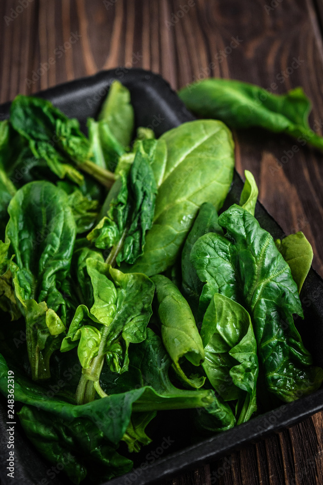 Leaves of spinach. Fresh organic spinach on a wooden table. Vegan food, healthy food. Dark rustic style photo. Leaves of spinach. Fresh organic spinach on a wooden table. Vegan food, healthy food. Dark rustic style photo.