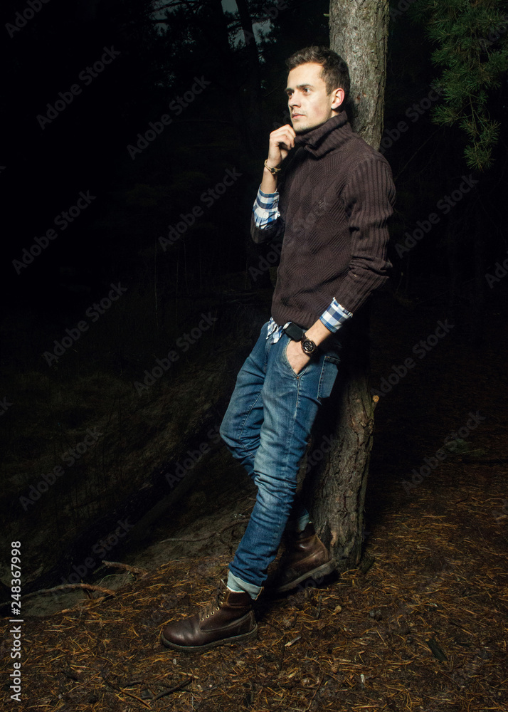 Handsome young man in the forest. A man in warm light poses at night in the woods