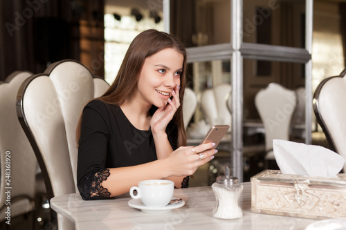 Young beautiful girl in black dress sits in a cafe and drinks coffee.