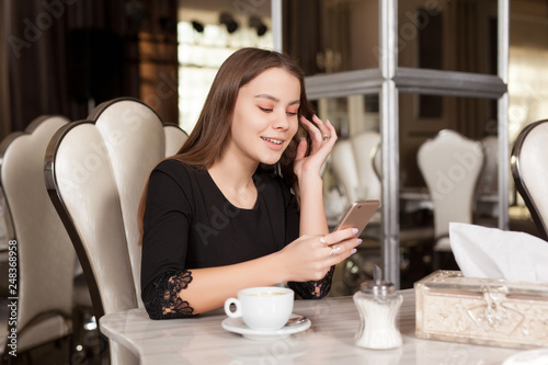 Young beautiful girl in black dress sits in a cafe and drinks coffee.