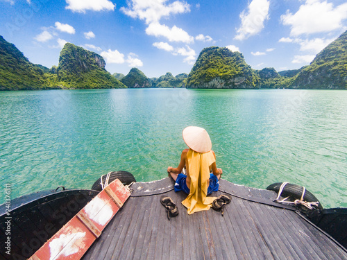 man wearing a Vietnamese hat enjoying the magnifiecent sight of Ha Long bay limestone rocks on a beautiful sunny day during a boat cruise, Vietnam photo