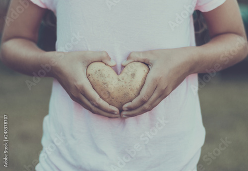 Woman holding heart shaped potato in front of stomach. Symbol of healthy lifestyle.