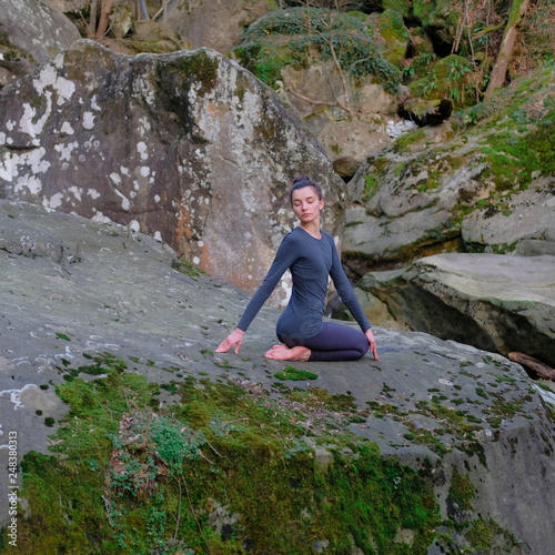 Young slim woman practicing yoga outdoors on big moss rock. Unity with nature concept. Girl in seated spinal twist pose