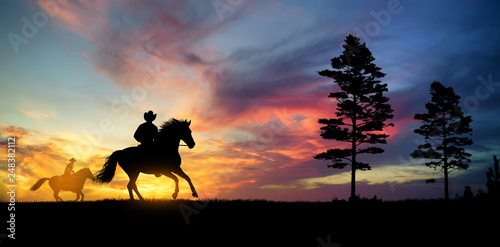A silhouette of two cowboy and horse at sunset