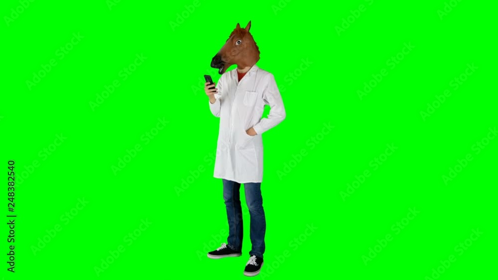 Hilarious Doctor in Horse Head Mask Standing on a Green Screen Checking Phone Hilarious Doctor in Horse Head Mask Standing on a Green Screen Checking Phone
