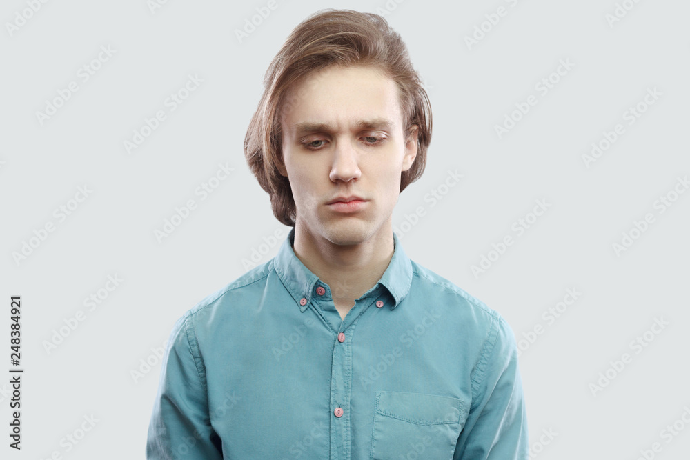 closeup portrait of sad worried handsome long haired blonde young man in blue casual shirt standing, holding head down and thinking what to do. indoor studio shot, isolated on light grey background. closeup portrait of sad worried handsome long haired blonde young man in blue casual shirt standing, holding head down and thinking what to do. indoor studio shot, isolated on light grey background.