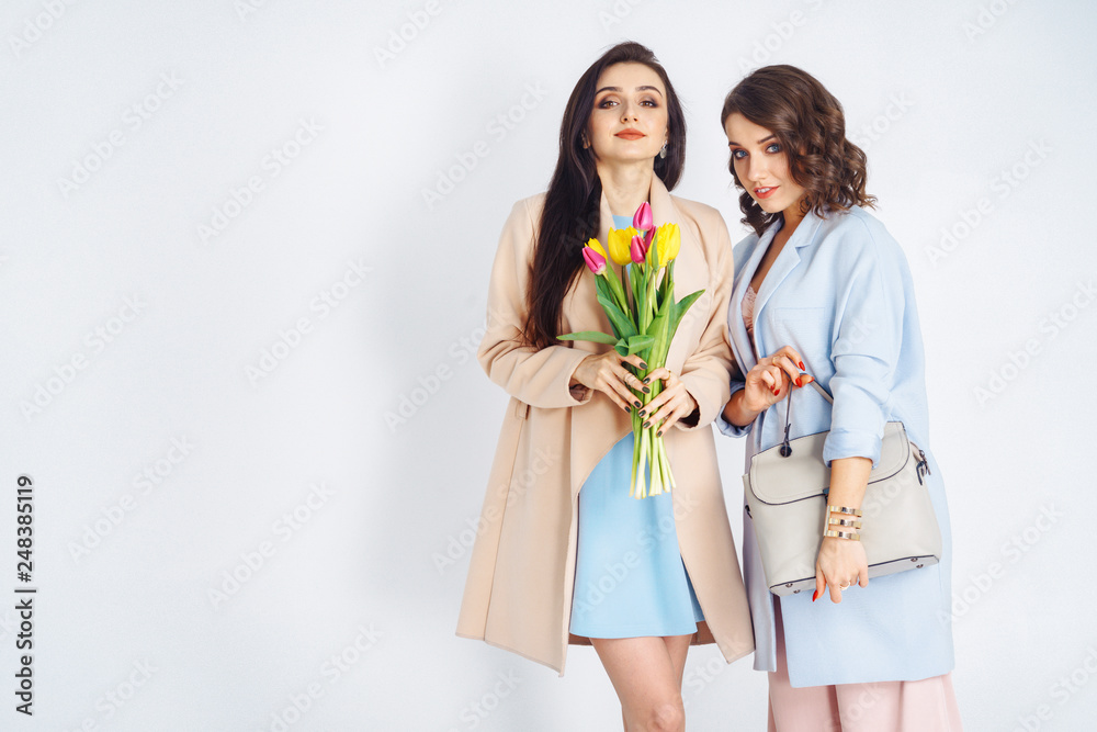 Fashion photo of two beautiful young women with tulips in the hand .they dressed in a beautiful coat, and T-shirt with stripes.Spring concept.March 8. beautiful girls in stylish clothes Fashion photo of two beautiful young women with tulips in the hand .they dressed in a beautiful coat, and T-shirt with stripes.Spring concept.March 8. beautiful girls in stylish clothes