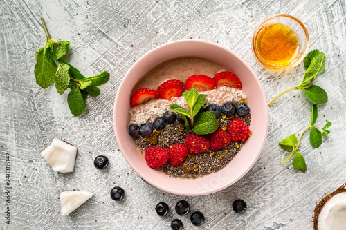 Closeup bowl of healthy oatmeal cereal with strawberry, raspberry, blueberry, mint, chia seeds and coconut at stone table background.