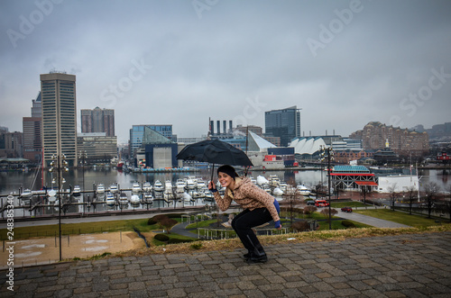 Young woman hides under an umbrella on a gloomy, rainy day in Inner Harbor Baltimore