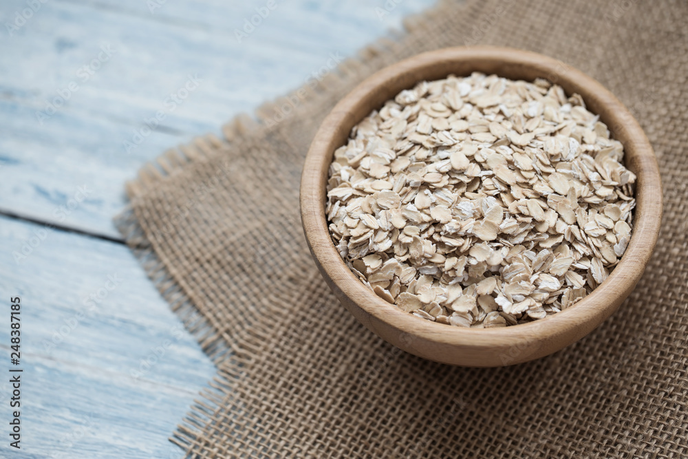 Uncooked oatmeal or oat flakes in a wooden bowl on a blue wooden background