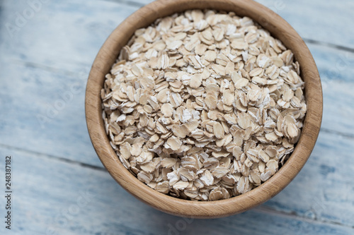 Uncooked oatmeal or oat flakes in a wooden bowl on a blue wooden background