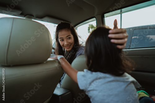 portrait of young asian mother driving a car and looking back at her daughter sitting behind