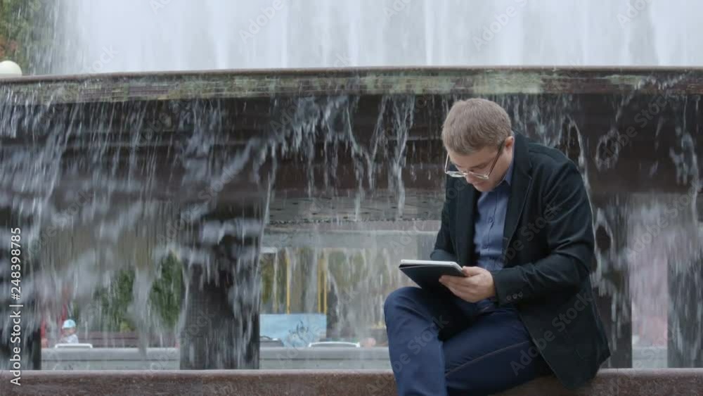 Man In Suit Working With Tablet Near Fountain Man In Suit Working With Tablet Near Fountain