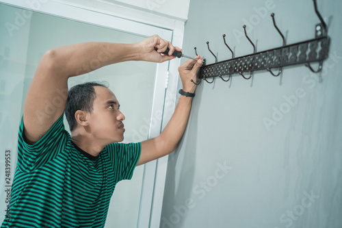 portrait of asian young man work with screwdriver to install a hangers on the wall