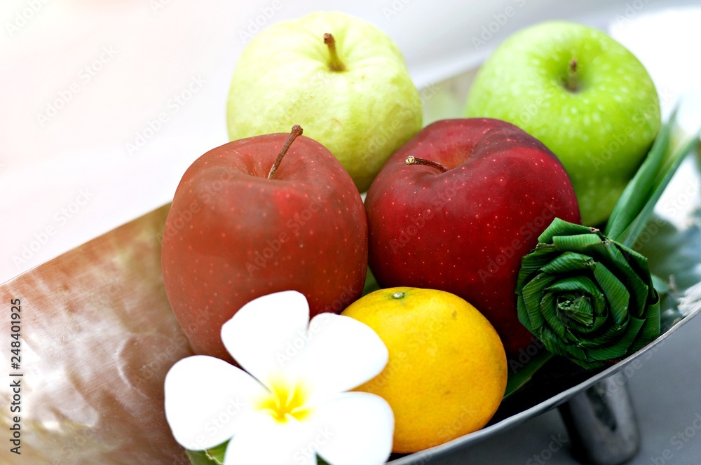 Close-up of ripe apples, oranges and guava served on tray at the wooden table, outdoor with sun light form nature