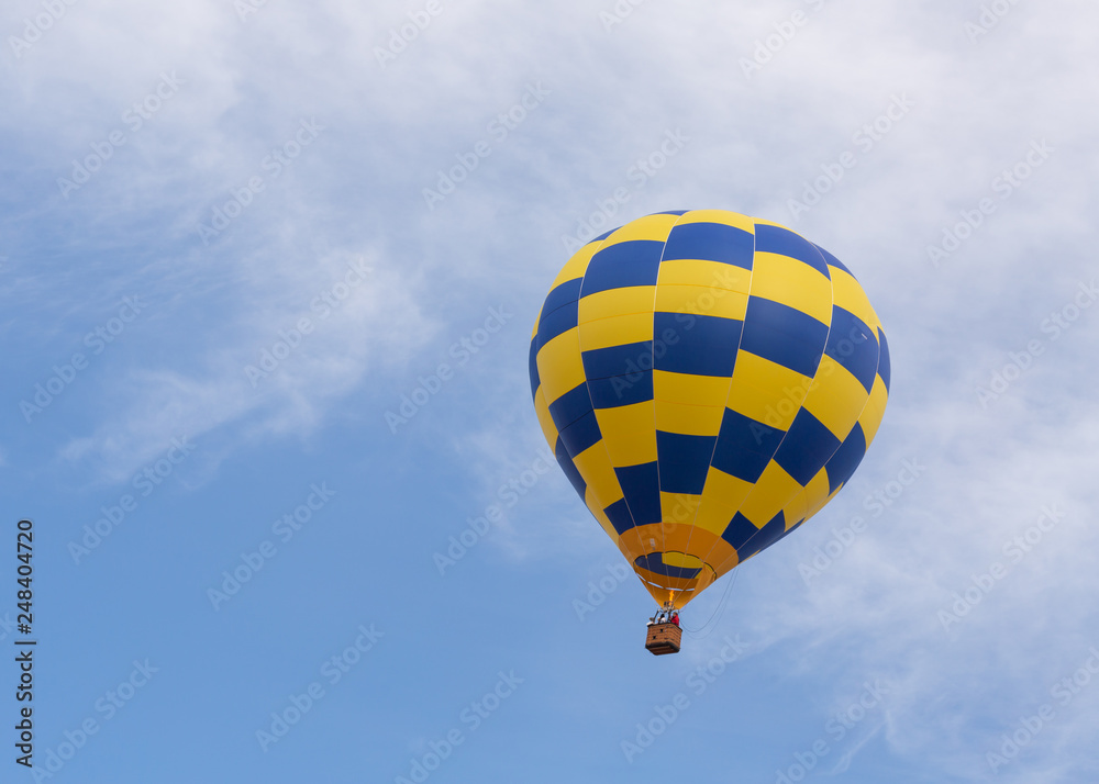 Naklejka premium A blue and yellow hot air balloon rises into a blue sky with wispy white clouds
