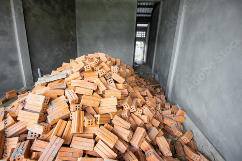 Red clay bricks are stacked on ground inside under construction house.