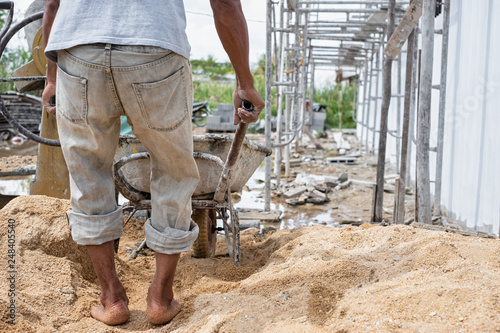 Construction worker pull wheelbarrow. Ready cement in wheelbarrow. Cement mixer machine equipment in construction site.