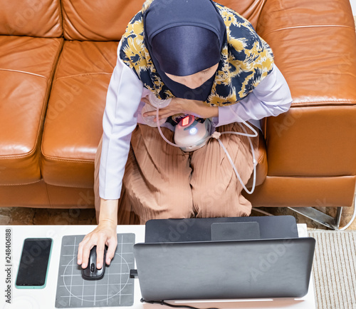 Busy young modern mother working with laptop while using automatically electric breast pump feeding for her baby. Top view.