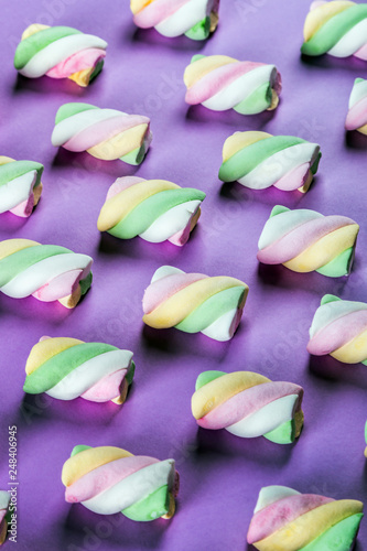 Colorful marshmallow is laid out on a purple paper background. pastel shades textured pattern