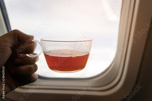 Hand hold cup of tea after meal and looking out of airplane, good time enjoying beautiful sky. 