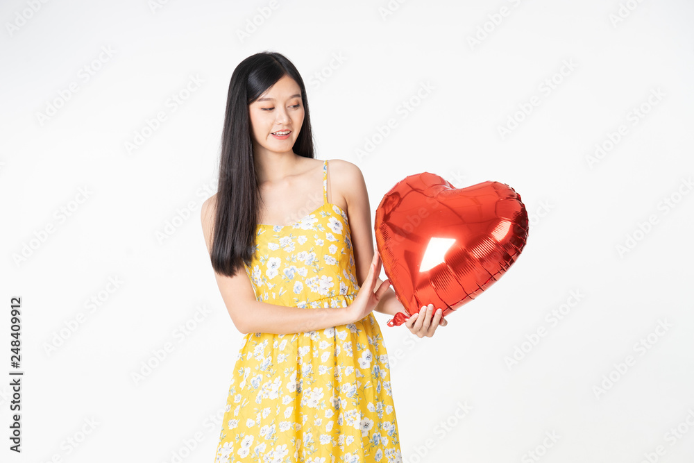Asian young woman in yellow dress hold red balloon heart. Young woman holding it with being excited and surprised holiday present isolated white background.concept love surprise valentine day. Asian young woman in yellow dress hold red balloon heart. Young woman holding it with being excited and surprised holiday present isolated white background.concept love surprise valentine day.
