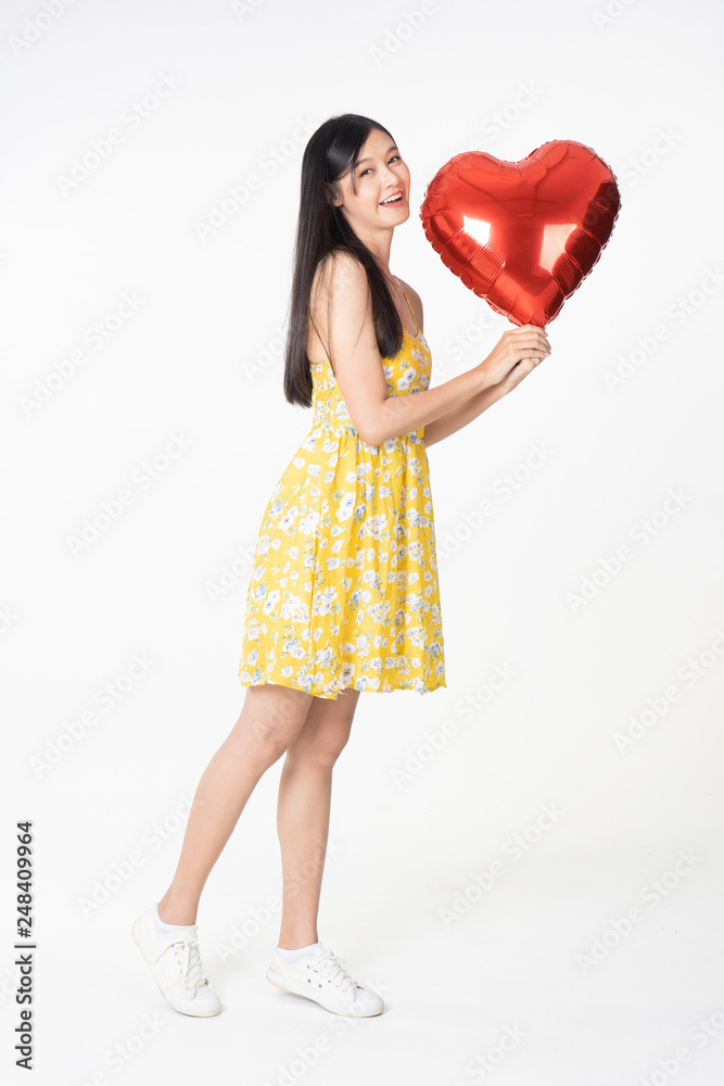 Asian young woman in yellow dress hold red balloon heart. Young woman holding it with being excited and surprised holiday present isolated white background.concept love surprise valentine day. Asian young woman in yellow dress hold red balloon heart. Young woman holding it with being excited and surprised holiday present isolated white background.concept love surprise valentine day.